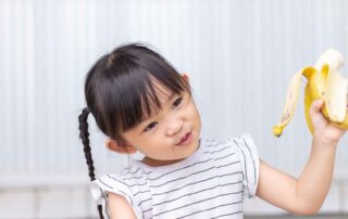 A young girl holding a peeled banana, engaged in a natural moment supporting early speech development