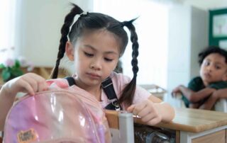 Young schoolgirl organizing her backpack in a classroom, representing the impact of speech therapy on academic readiness and communication confidence